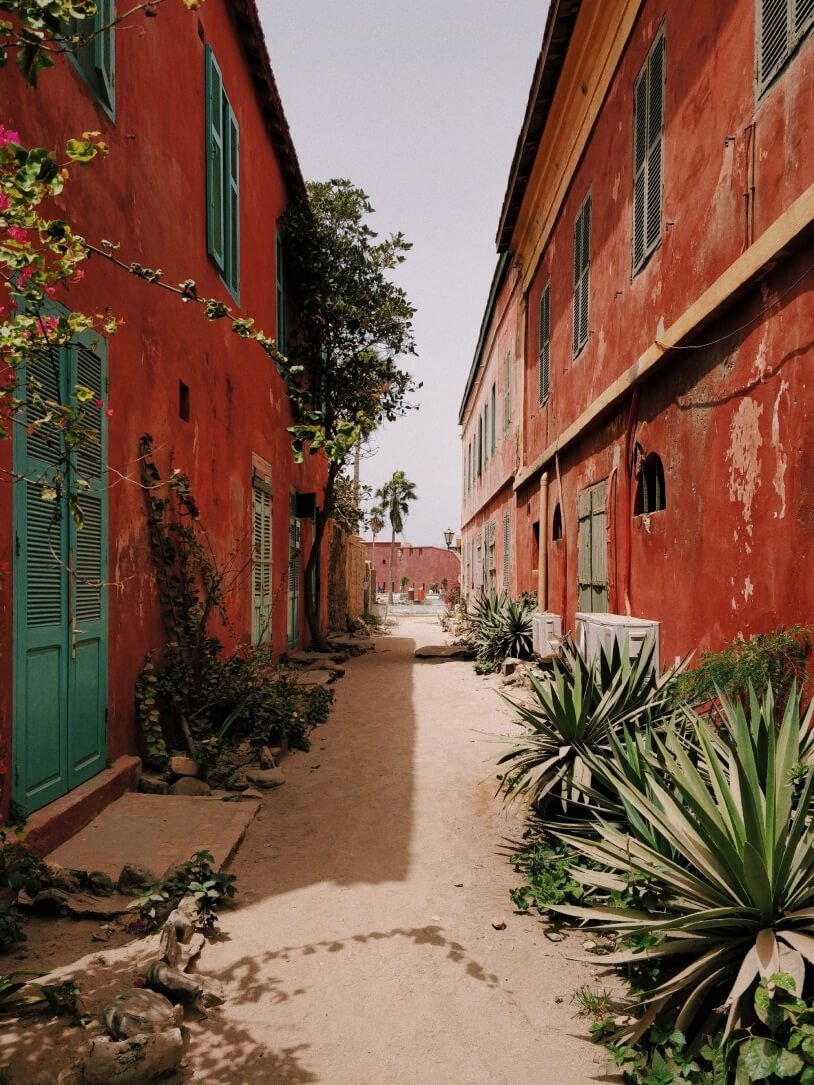 A sandy lane between two red houses with green shutters